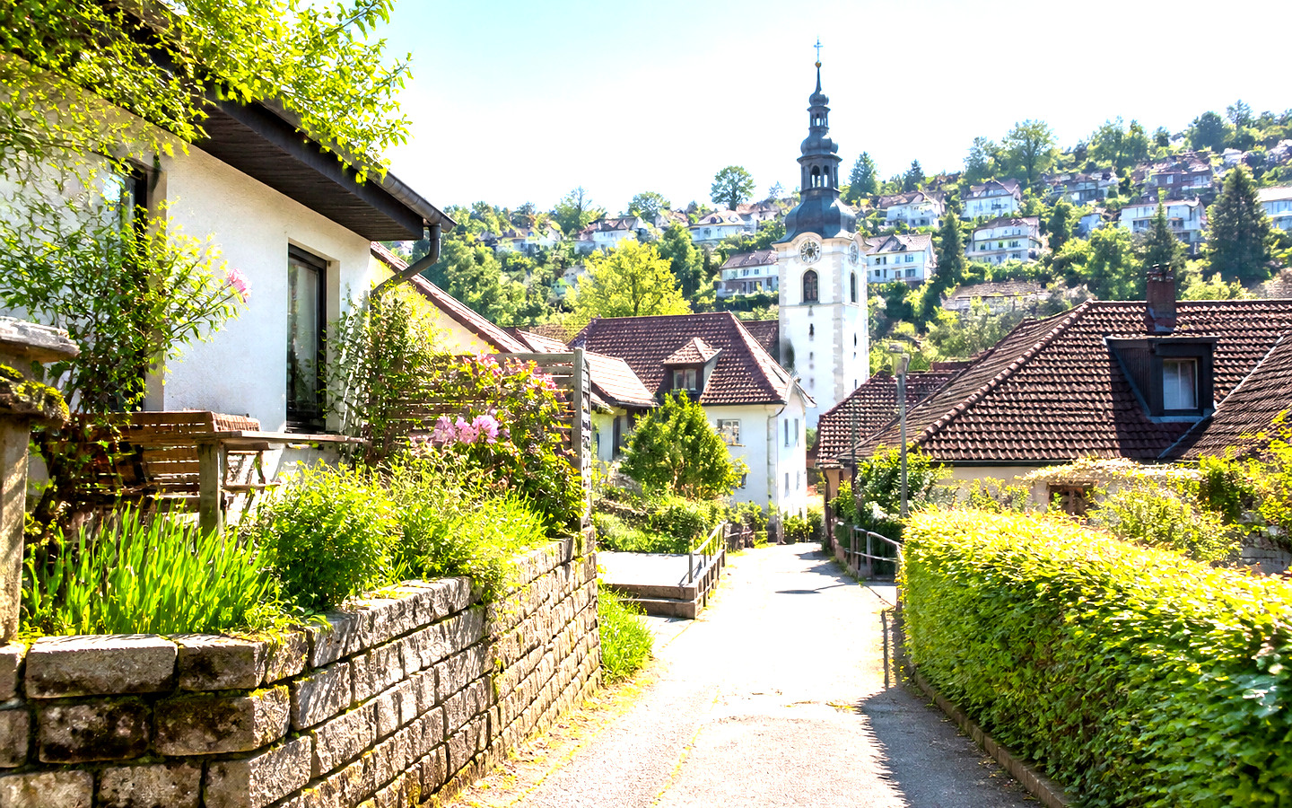 Weg zwischen Häusern und Gärten mit einem Kirchturm